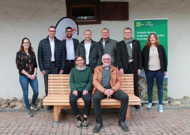 Geschäftsleiterin Christine Neff und Vizepräsident Ruedi Lüscher vom Jurapark auf dem Bänkli sitztend, umringt von den Sponsoren von Raiffeisenbank und Coop, anlässlich der Einweihung vor der alten Effinger Trotte. Foto: Sonja Fasler
