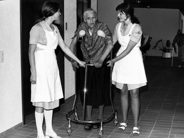 Historisches Bild aus dem Archiv: Zwei Pflegehelferinnen SRK stützen eine alte Frau beim Gehen. Copyright: Archiv SRK, Foto: Margrit Hofer